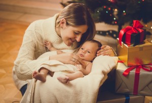 mother kissing baby boy lying in living room decorated for Chris